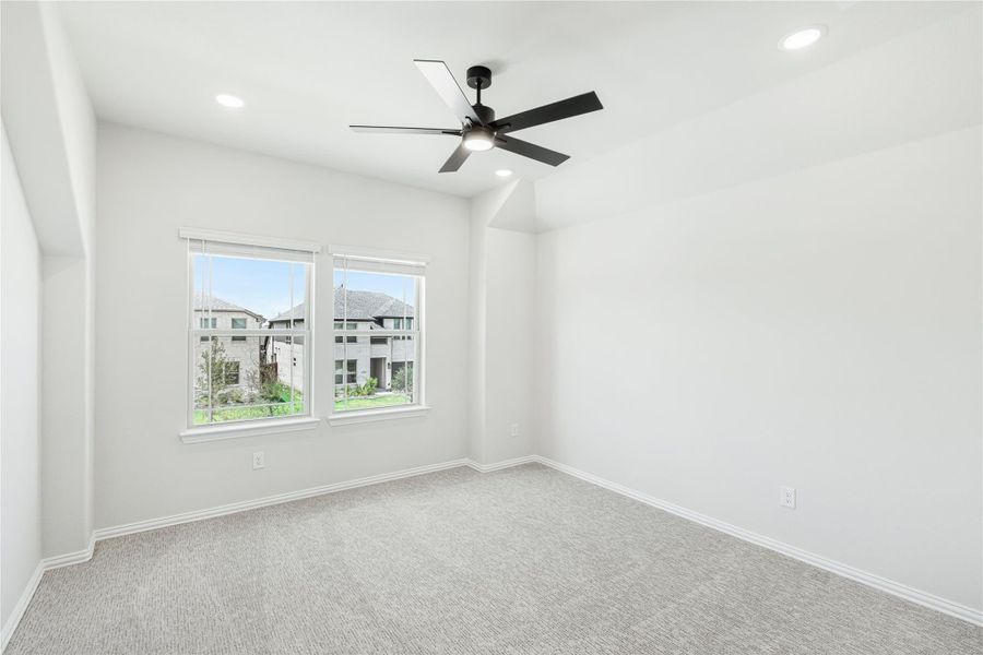 Empty bedroom with gray carpet, black ceiling fan, and two windows with neighborhood view