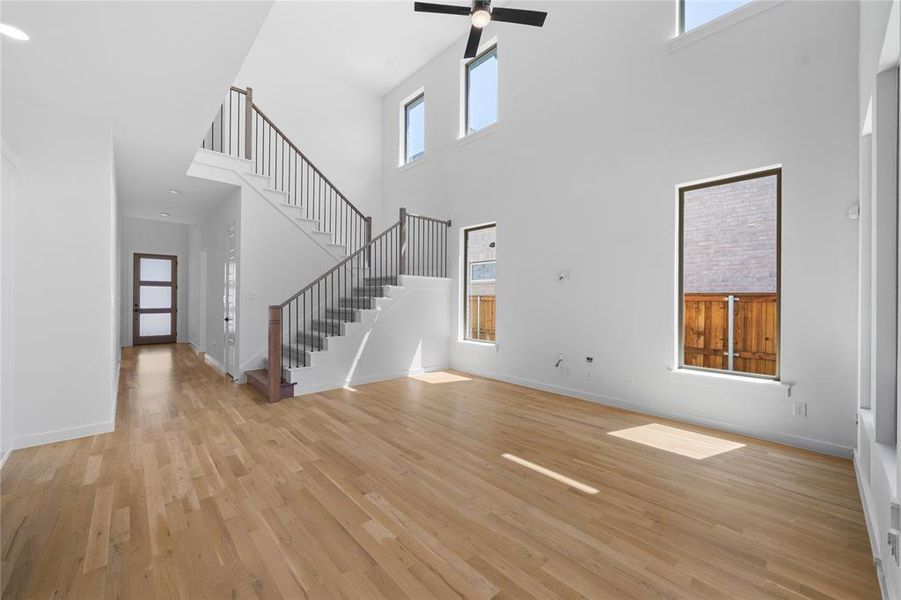 Two-story living area featuring a prominent staircase with dark wood handrails and metal balusters, high ceilings, large windows, wood-finish flooring, and a modern ceiling fan