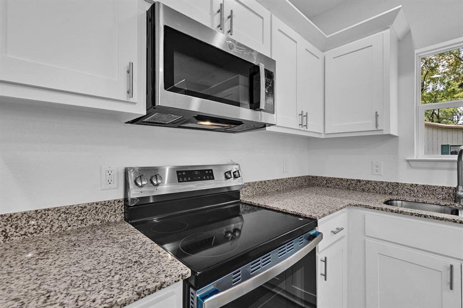 Kitchen featuring appliances with stainless steel finishes, white cabinets, and light stone countertops Kitchen featuring appliances with stainless steel finishes, white cabinets, and light stone countertops