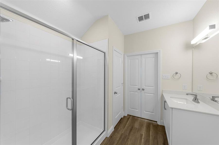 Contemporary bathroom featuring a glass-enclosed shower with white subway tile, a vanity with a white countertop and integrated sink, a large wall mirror, and wood-finish flooring