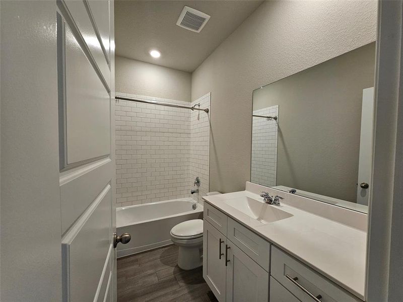 Bathroom featuring vanity, tile wall, wood looking tile floors, tub / shower combination, and recessed lighting.