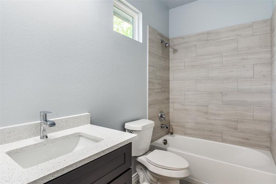 Full bathroom featuring vanity, tiled shower / bath combo, and toilet