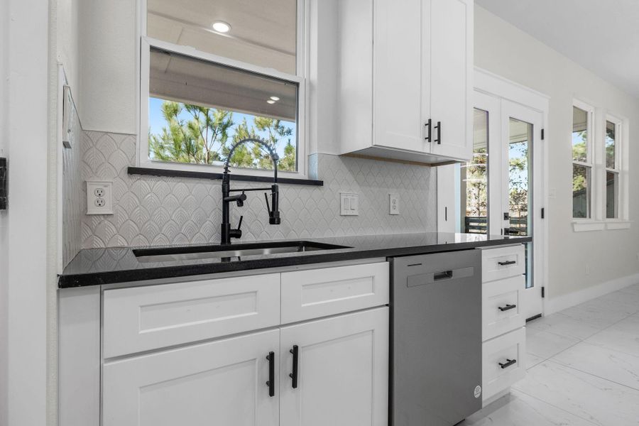 Kitchen featuring sink, stainless steel dishwasher, white cabinetry, and decorative backsplash