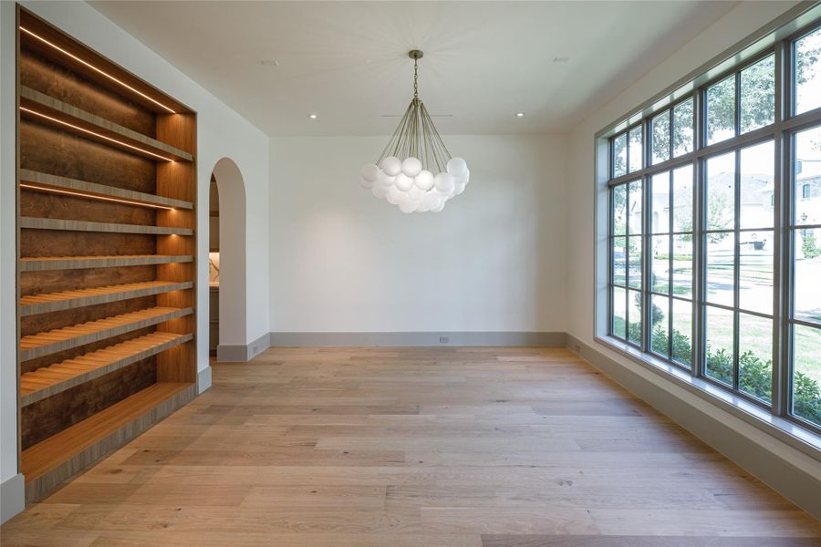 The dining room makes its own statement. A sculptural globe chandelier hangs opposite a dramatic wall of divided-light windows, while a custom illuminated wine display turns the collection into part of the architecture.