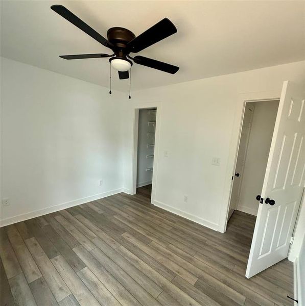 Unfurnished bedroom with a ceiling fan, wood finished floors, and a spacious closet
