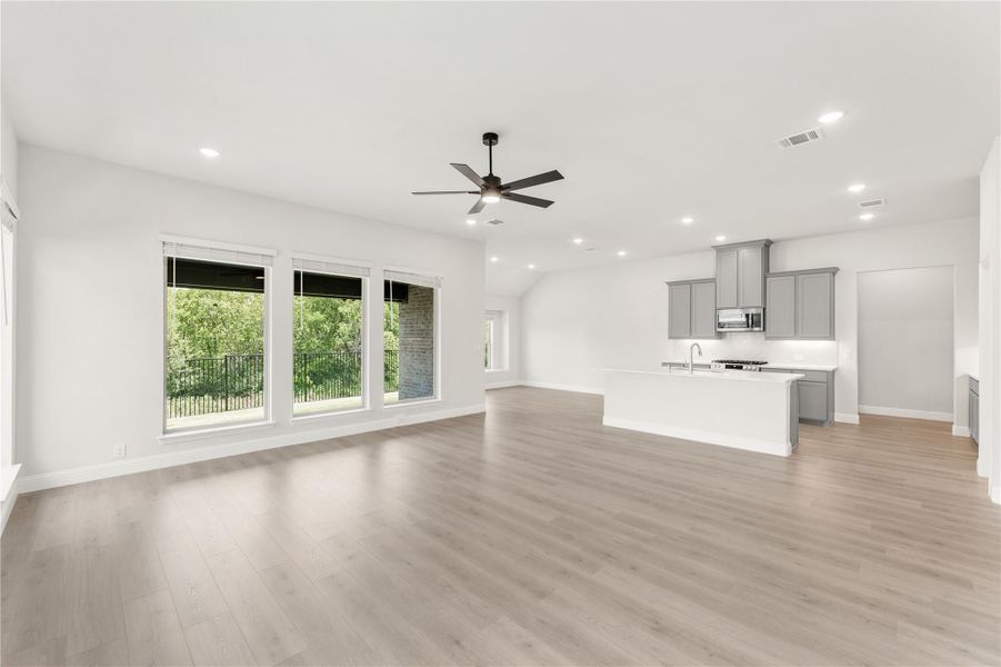 Open living area with light wood floors, ceiling fan, and kitchen with gray cabinets and white island Open living area with light wood floors, ceiling fan, and kitchen with gray cabinets and white island
