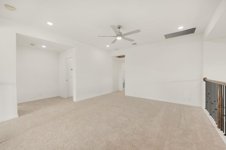Open upstairs loft with beige carpet, ceiling fan, and staircase railing along one wall.