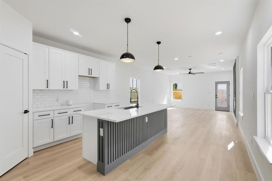 Kitchen featuring a center island with sink, pendant lighting, white cabinetry, and light wood-style floors