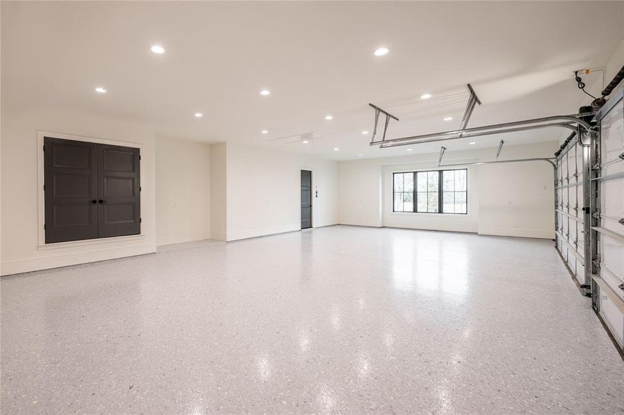 Spacious garage featuring an epoxy floor, recessed lighting, large windows with black trim, and two dark paneled doors