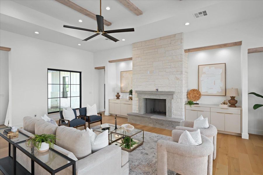 Living room with light wood-type flooring, recessed lighting, ceiling fan, a stone fireplace, and beam ceiling