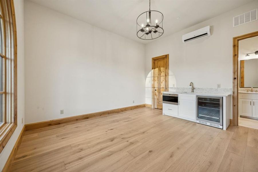 Unfurnished living room with wine cooler, light wood-style floors, a chandelier, and a wall mounted air conditioner