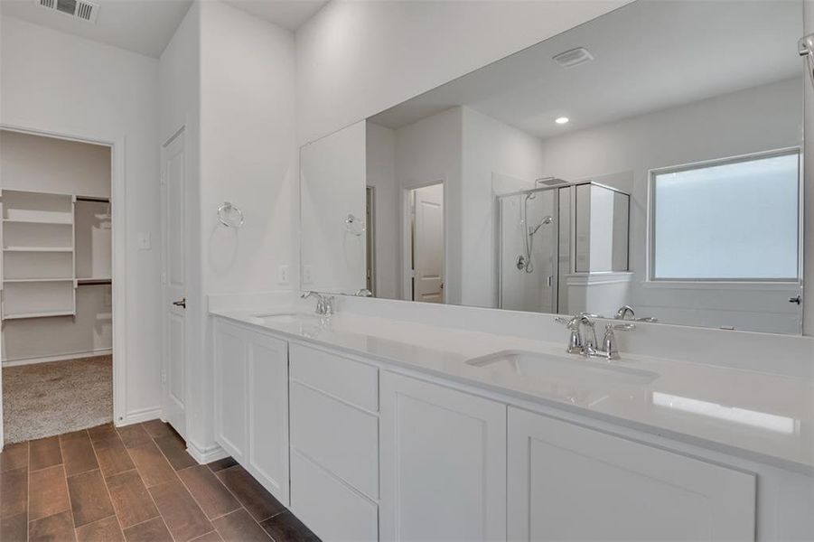 Primary Bathroom featuring vanity with extensive cabinet space, an enclosed shower, and double sink