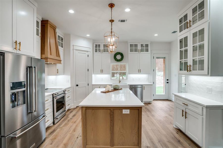 Kitchen featuring a center island, white cabinets, light wood-type flooring, decorative light fixtures, and stainless steel appliances