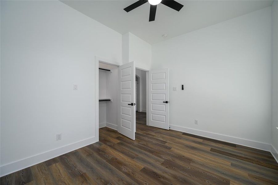 Unfurnished bedroom with dark wood-type flooring, ceiling fan, and a high ceiling