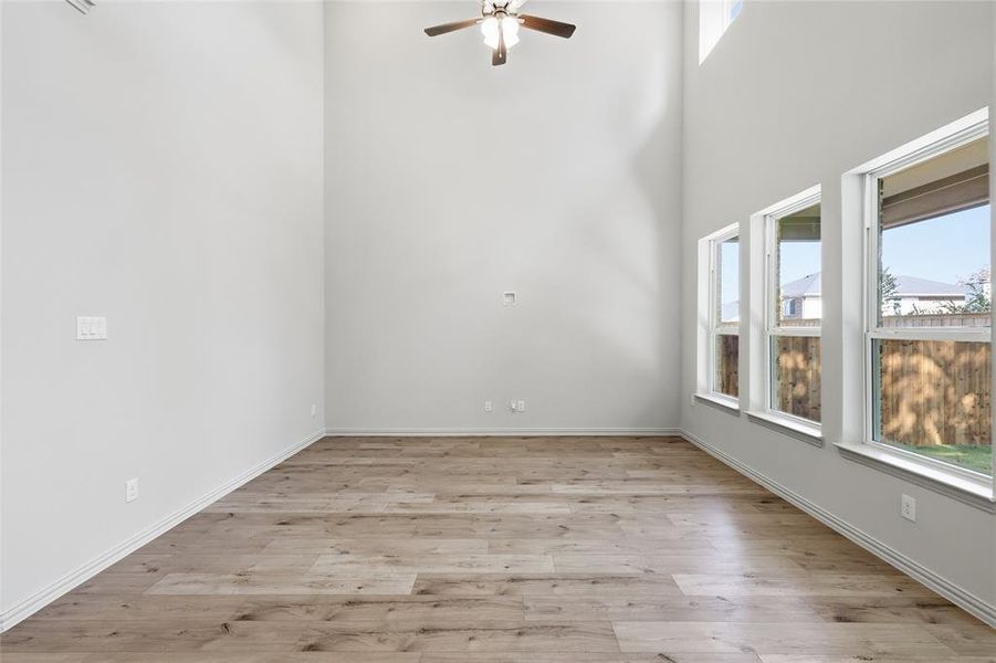Empty room with plenty of natural light, light wood-style floors, a high ceiling, and a ceiling fan