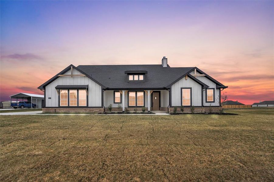 Modern farmhouse style home featuring board and batten siding, roof with shingles, a porch, a chimney, and a yard