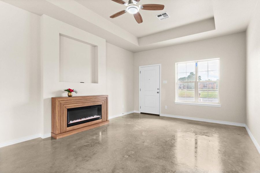 Unfurnished living room with a glass covered fireplace, finished concrete flooring, a raised ceiling, and a ceiling fan