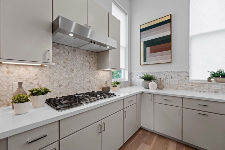 Kitchen featuring a built-in gas range, stainless steel range hood, stone hexagonal mosaic tile backsplash, light-toned cabinetry, and solid surface countertops