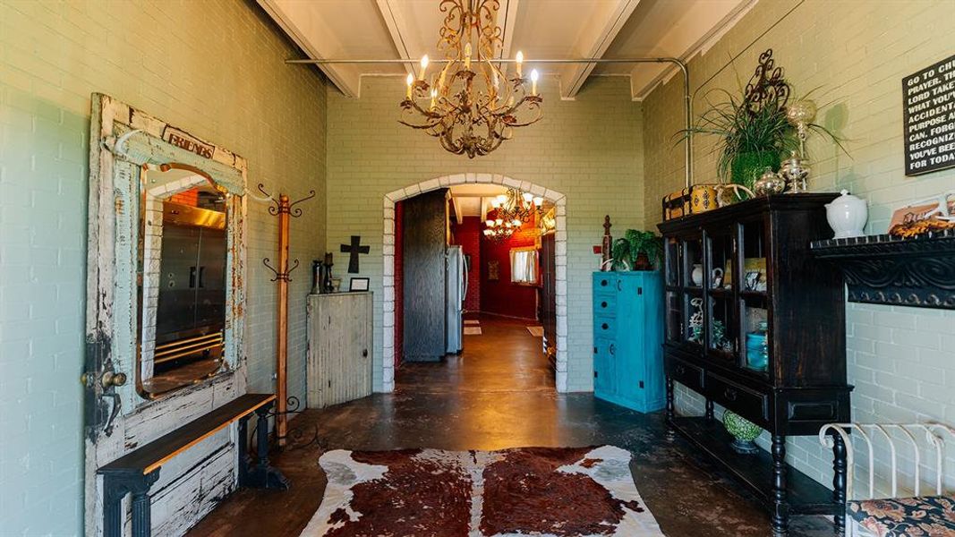 Foyer with a towering ceiling, arched walkways, finished concrete floors, a chandelier, and brick wall