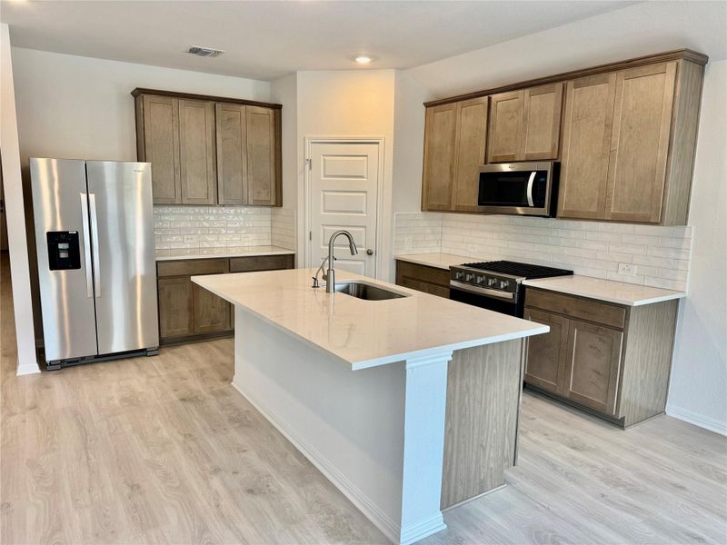 Kitchen with backsplash, appliances with stainless steel finishes, light wood-type flooring, a center island with sink, and recessed lighting Kitchen with backsplash, appliances with stainless steel finishes, light wood-type flooring, a center island with sink, and recessed lighting