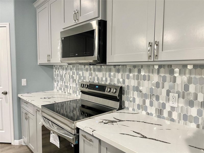 A well-appointed kitchen features quartz countertops and an eye-catching geometric tile backsplash.