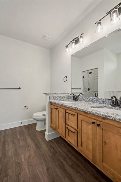 Full bathroom with a marble finish shower, double vanity, and dark wood-style flooring