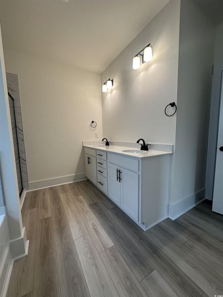 Full bath with double vanity, light wood-style flooring, and an enclosed shower