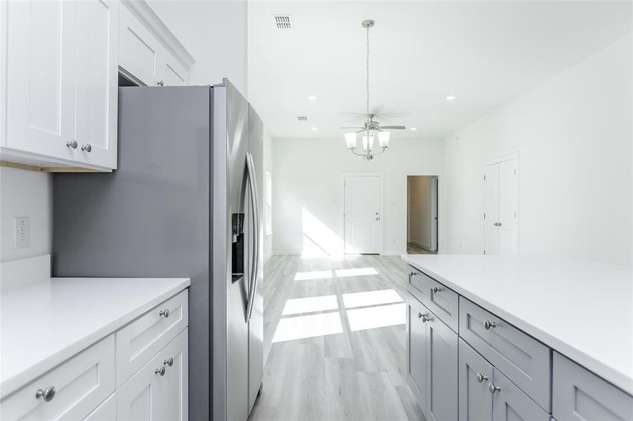 Kitchen featuring stainless steel fridge, white cabinetry, light wood-type flooring, decorative light fixtures, and ceiling fan