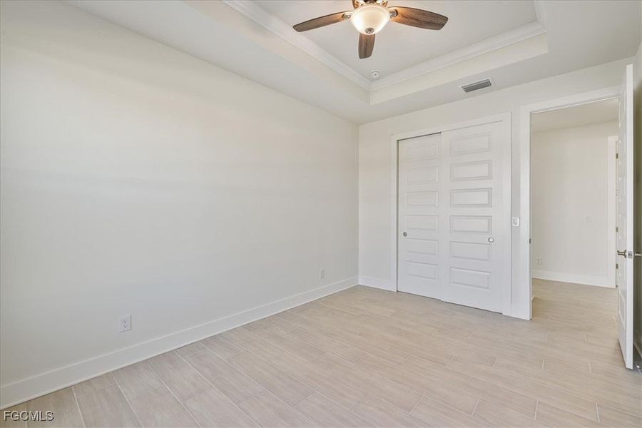 Unfurnished bedroom with a raised ceiling, light wood-type flooring, ceiling fan, a closet, and crown molding