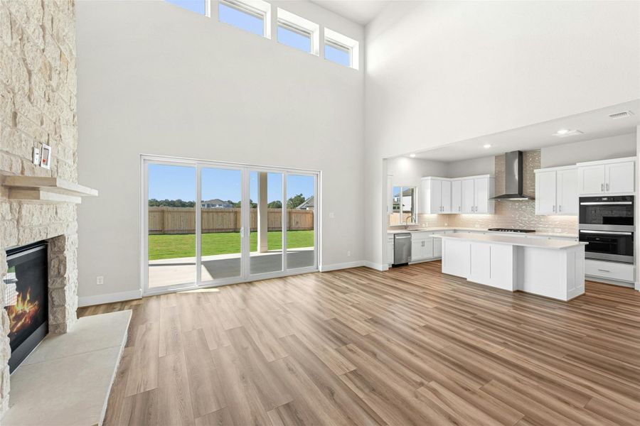 Kitchen with open floor plan, white cabinetry, light wood-style floors, a stone fireplace, and a towering ceiling