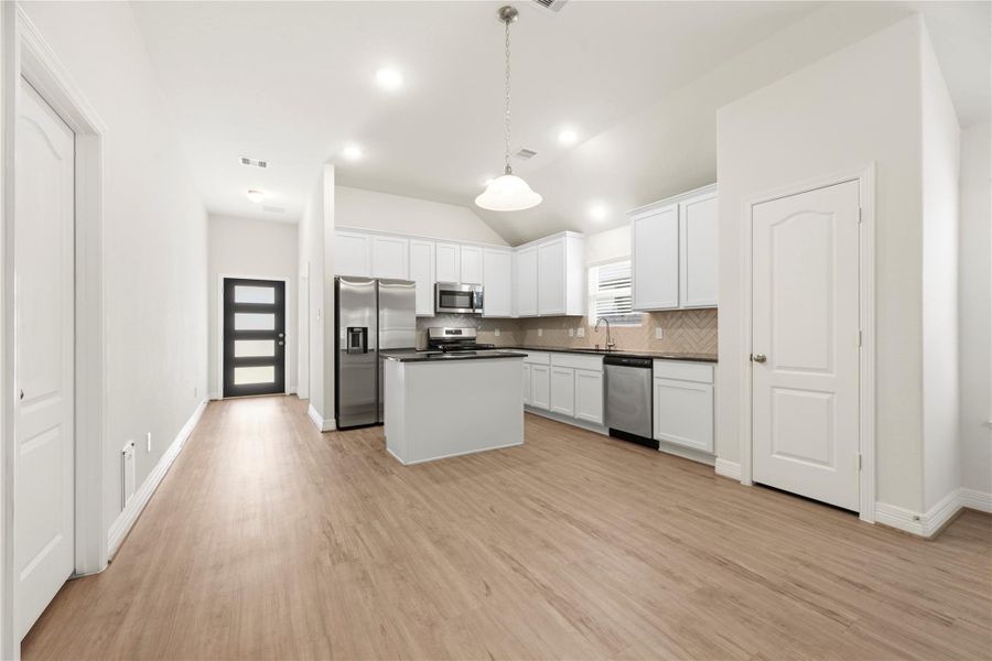 Bright, modern kitchen with stainless steel appliances, white cabinetry, and an island. The open layout features wood-look flooring and recessed lighting, offering a spacious and inviting feel.