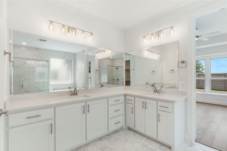Master bathroom with dual sinks, white cabinets, marble tile floors, and large mirrors with vanity lighting