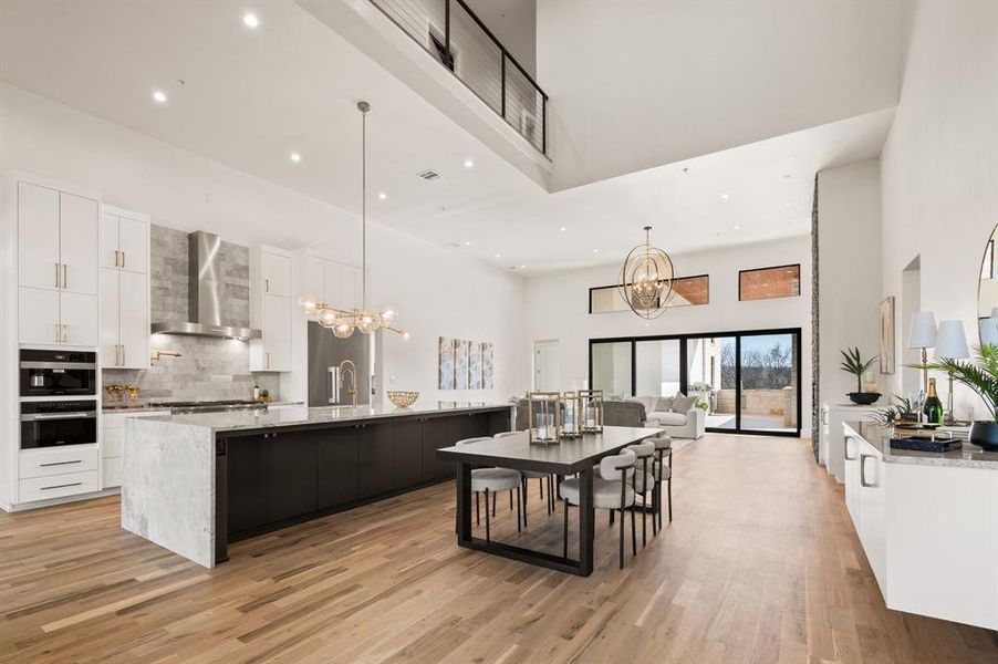 Kitchen with pendant lighting, wall chimney range hood, a notable chandelier, and a large island with sink