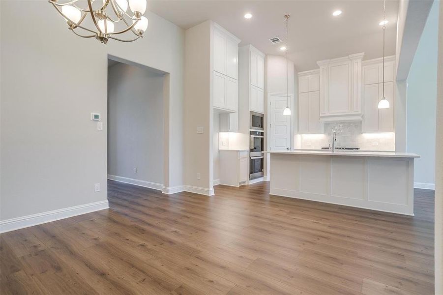 Kitchen with backsplash, light wood-type flooring, a kitchen island with sink, white cabinets, and hanging light fixtures