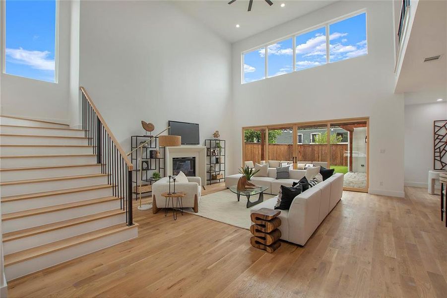 Living area featuring a high ceiling, a glass covered fireplace, light wood-style floors, stairway, and baseboards Living area featuring a high ceiling, a glass covered fireplace, light wood-style floors, stairway, and baseboards