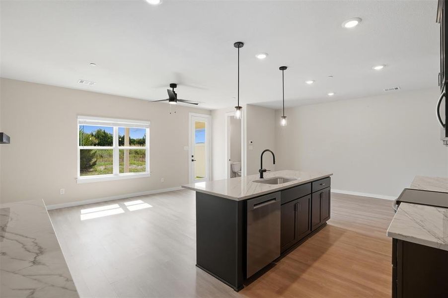Kitchen featuring light stone counters, open floor plan, light wood-type flooring, pendant lighting, and dishwasher Kitchen featuring light stone counters, open floor plan, light wood-type flooring, pendant lighting, and dishwasher
