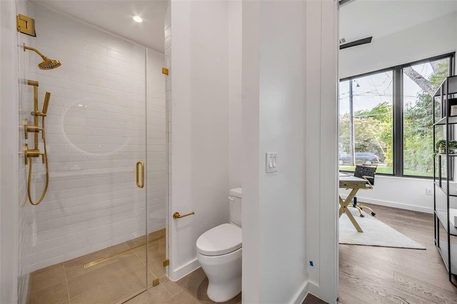 This stylish ensuite bathroom, accessible from the office/bedroom or the hall, features a sleek glass-enclosed shower and luxurious gold fixtures, adding elegance to both adjoining spaces.