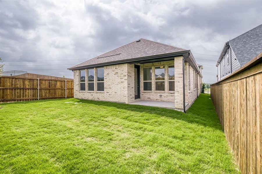 Spacious backyard featuring a covered patio, light brick exterior, dark frame windows, and a privacy fence