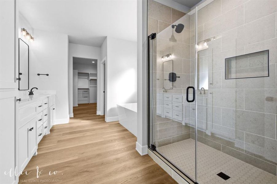 Bathroom featuring a soaking tub, a spacious closet, double vanity, light wood-style floors, and a stall shower