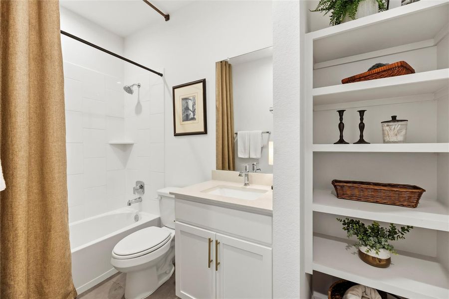 Full bathroom downstairs with upgraded gray porcelain tile flooring, a white vanity, tub and shower combination and built-in shelving.