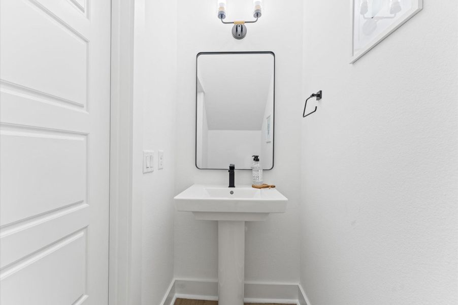 Chic and convenient, this first-floor powder room is thoughtfully positioned for guests and everyday ease. Featuring a stylish pedestal sink, warm lighting, and a statement mirror, the space blends function with flair. Chic and convenient, this first-floor powder room is thoughtfully positioned for guests and everyday ease. Featuring a stylish pedestal sink, warm lighting, and a statement mirror, the space blends function with flair.