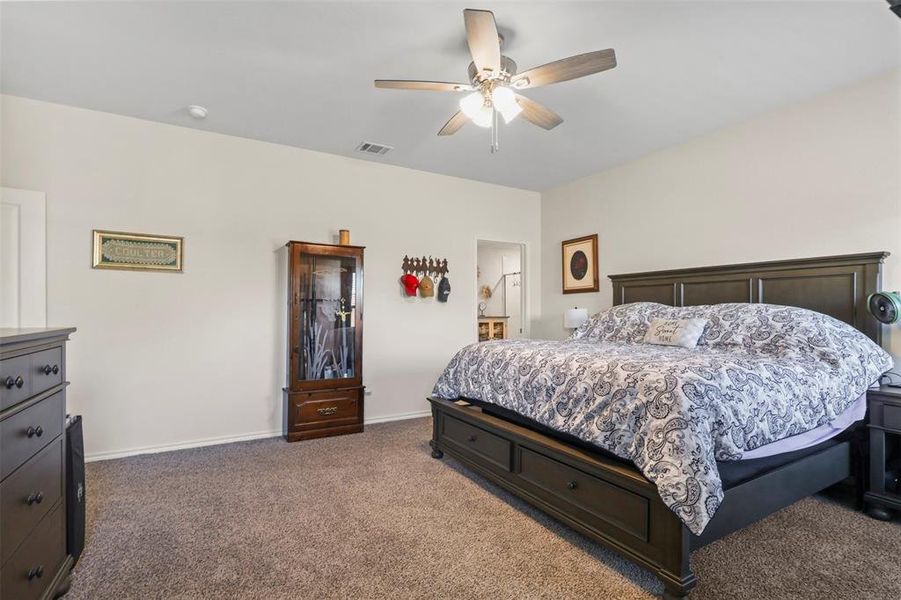 Bedroom with dark carpet, a ceiling fan, and ensuite bathroom