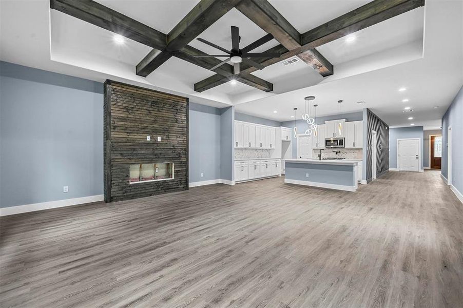 Unfurnished living room with beamed ceiling, a multi sided fireplace, ceiling fan, and light hardwood / wood-style floors