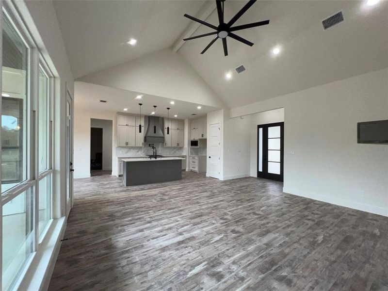 Spacious living area featuring wood-finish flooring, a vaulted ceiling with a modern ceiling fan, and recessed lighting