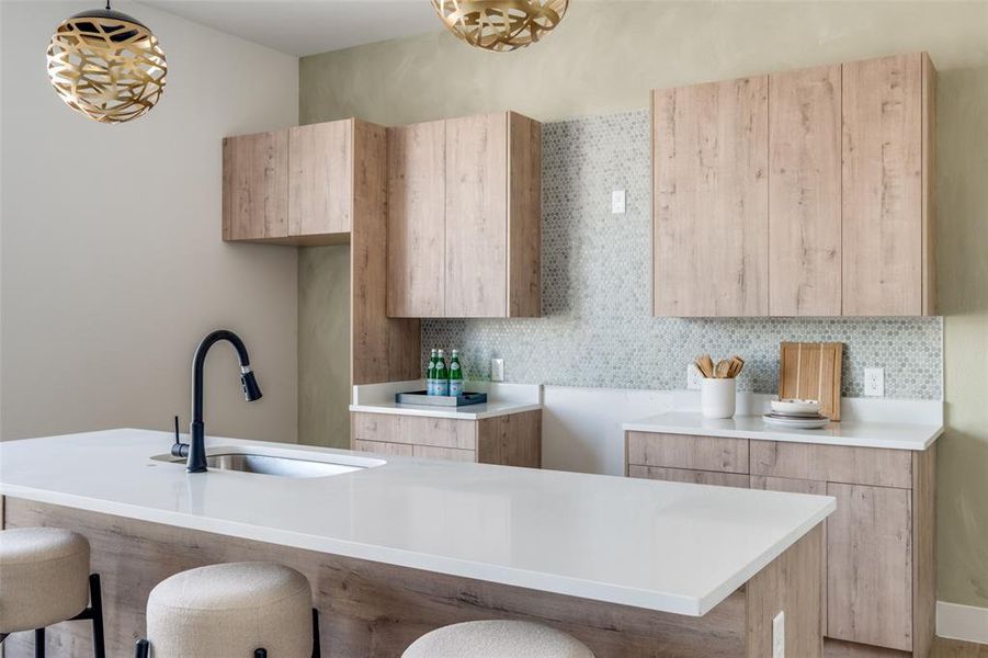 Kitchen featuring backsplash, a kitchen breakfast bar, sink, light brown cabinetry, and decorative light fixtures