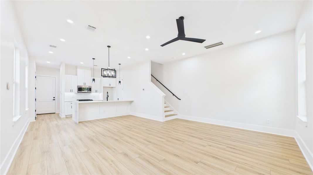 This photo showcases a spacious, open-concept living area with light wood flooring and recessed lighting. The kitchen features a large island with pendant lighting, sleek cabinetry, and stainless steel appliances. This photo showcases a spacious, open-concept living area with light wood flooring and recessed lighting. The kitchen features a large island with pendant lighting, sleek cabinetry, and stainless steel appliances.