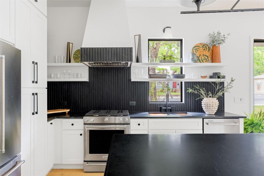 Kitchen with open shelves, dark countertops, white cabinets, a sink, and stainless steel appliances