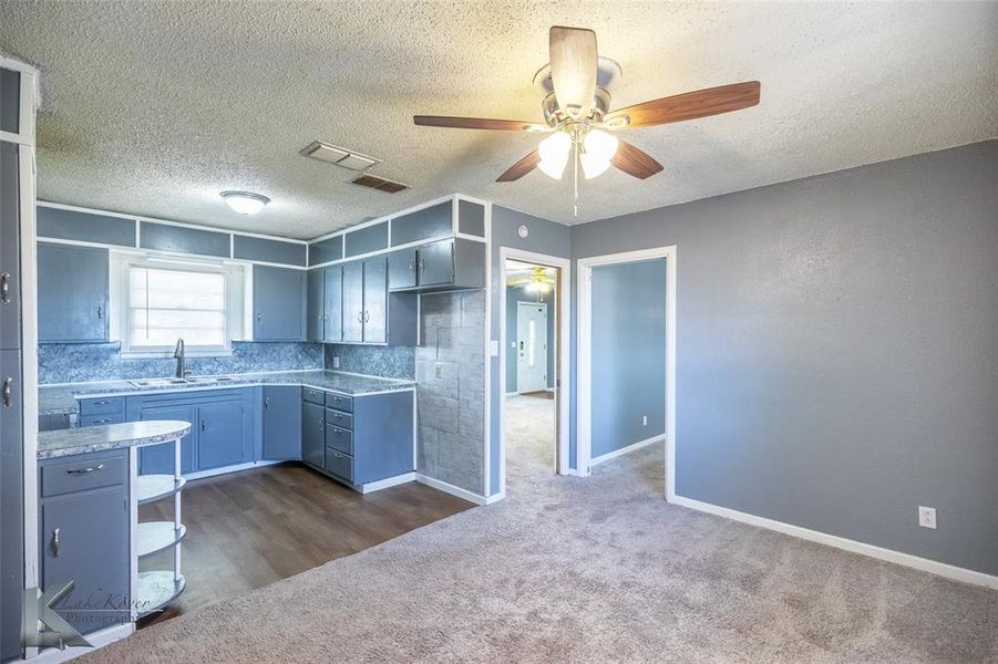 Kitchen with a textured ceiling, ceiling fan, dark carpet, light countertops, and decorative backsplash