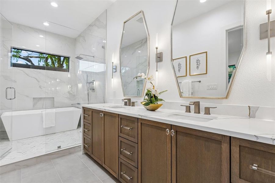 Spa-like primary bathroom with dual vanities, soaking tub, and glass-enclosed shower finished with elegant marble surfaces.