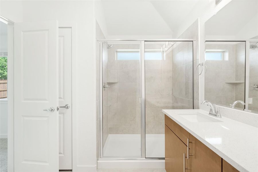Bathroom with glass-door walk-in shower, tile walls, and double vanity with white countertop